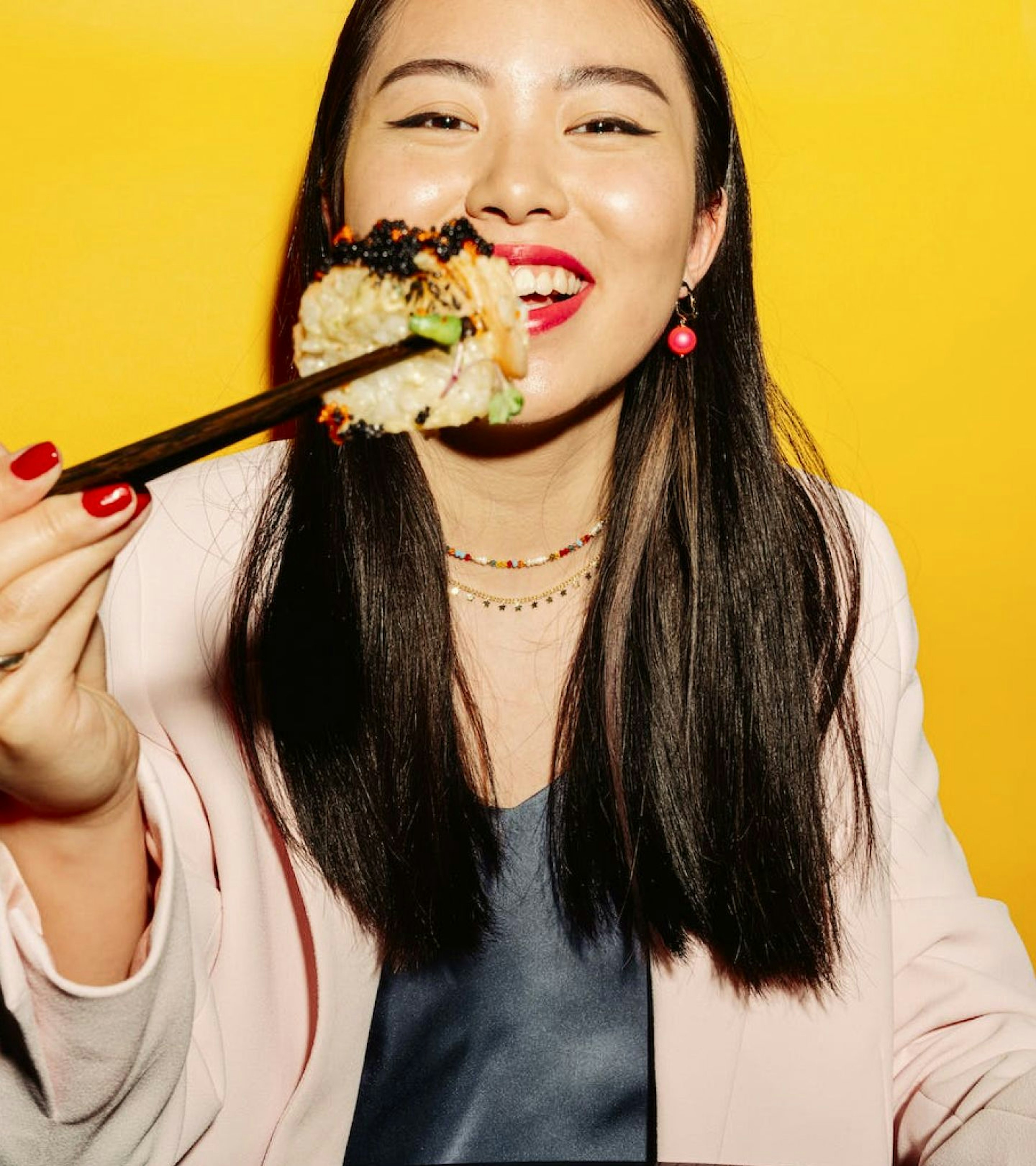 An image of a woman with dark hair eating a sushi roll