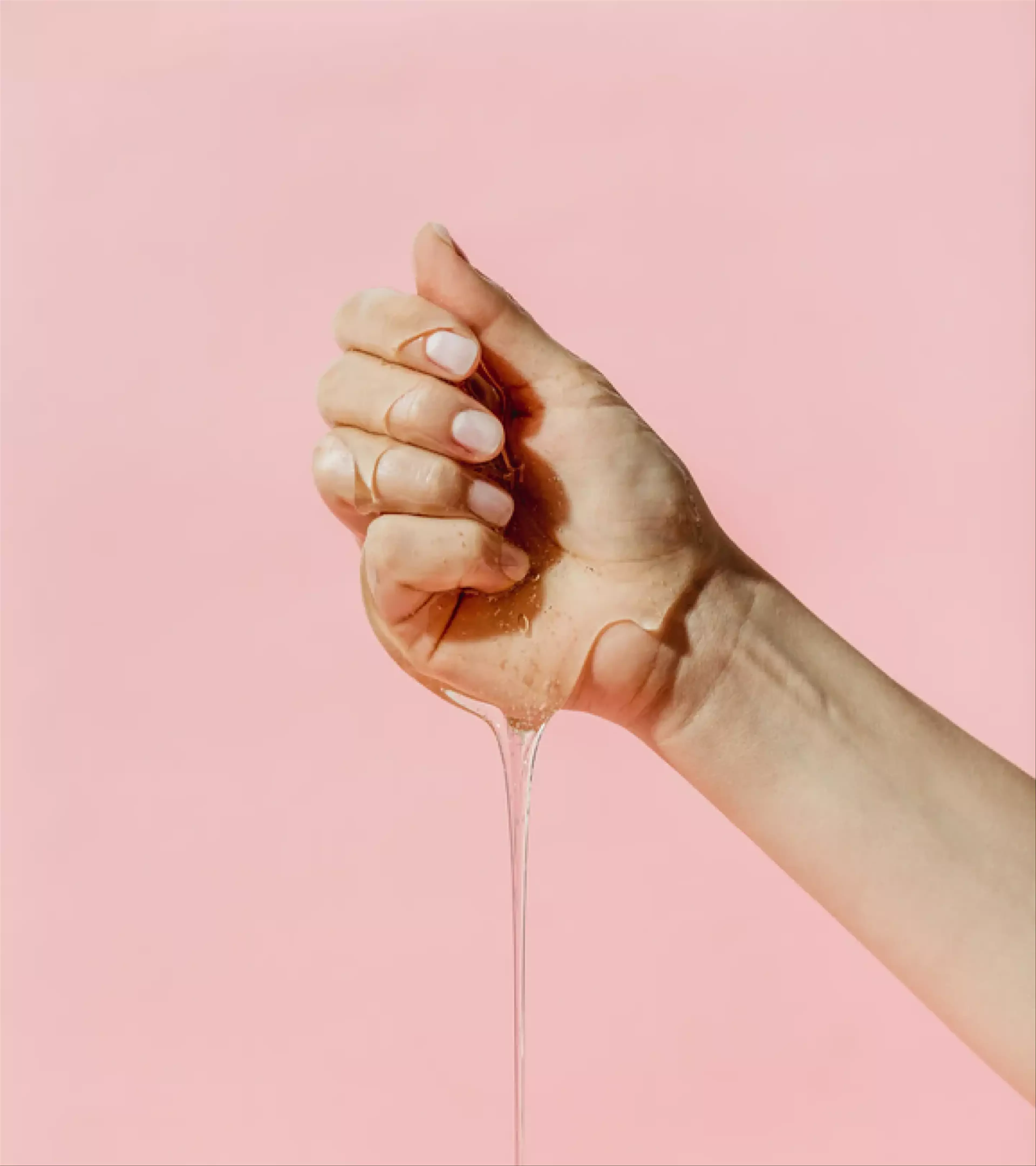 An image of a hand with lubricant on a pink background