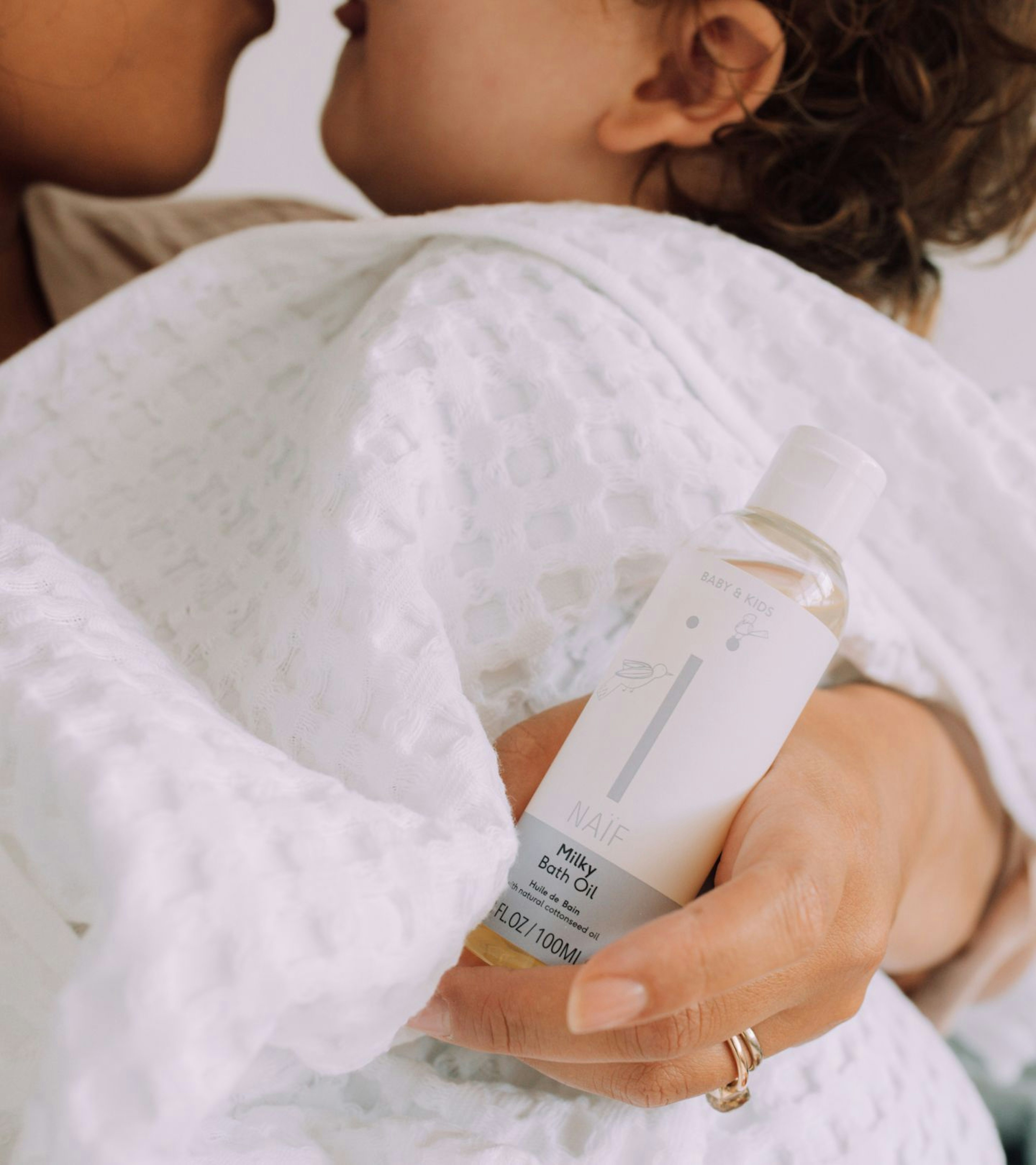 An image of a mother holding her son in a white cloth holding the milky bath oil product