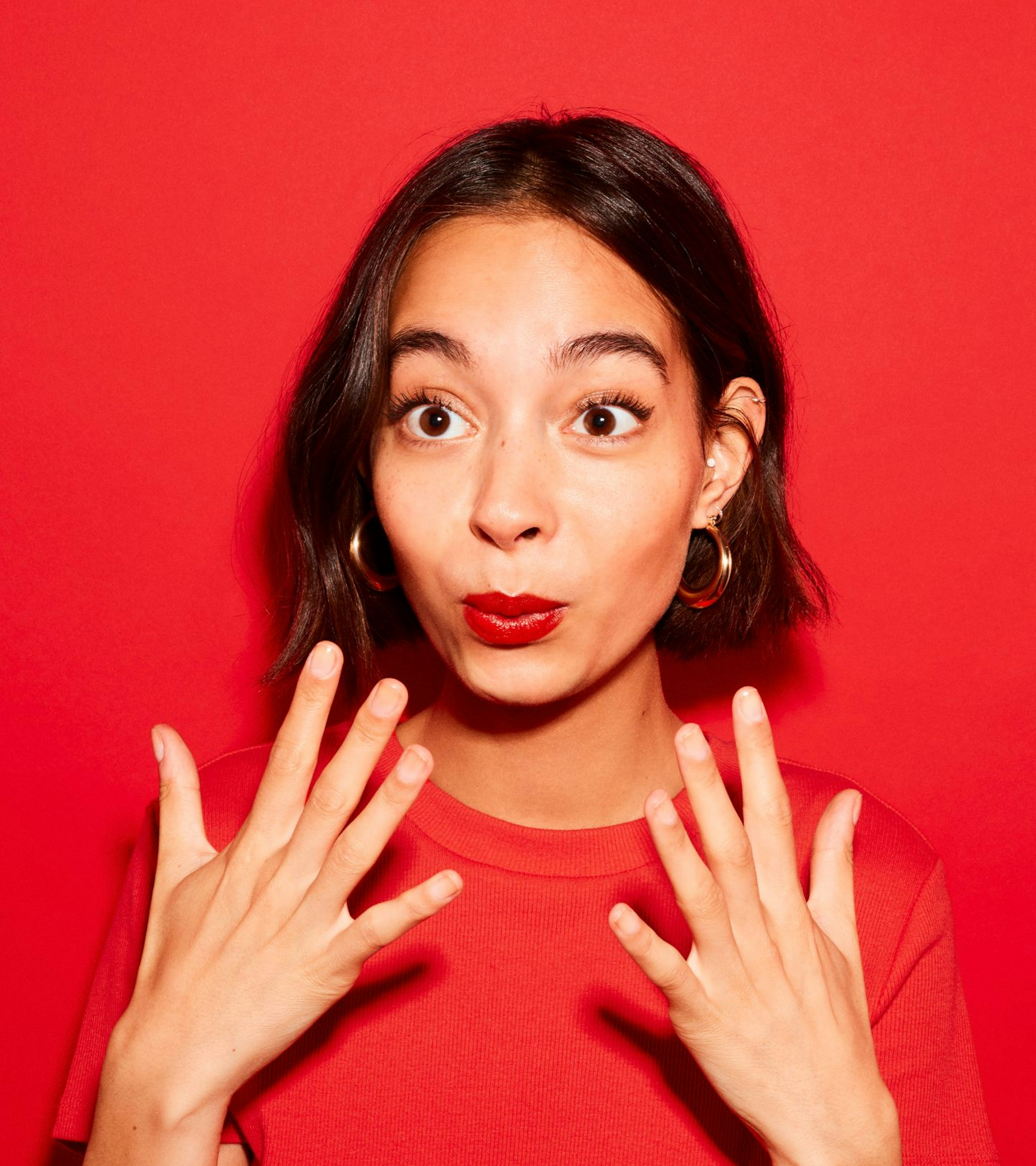 An image of a woman holding her hands to her mouth on a red background