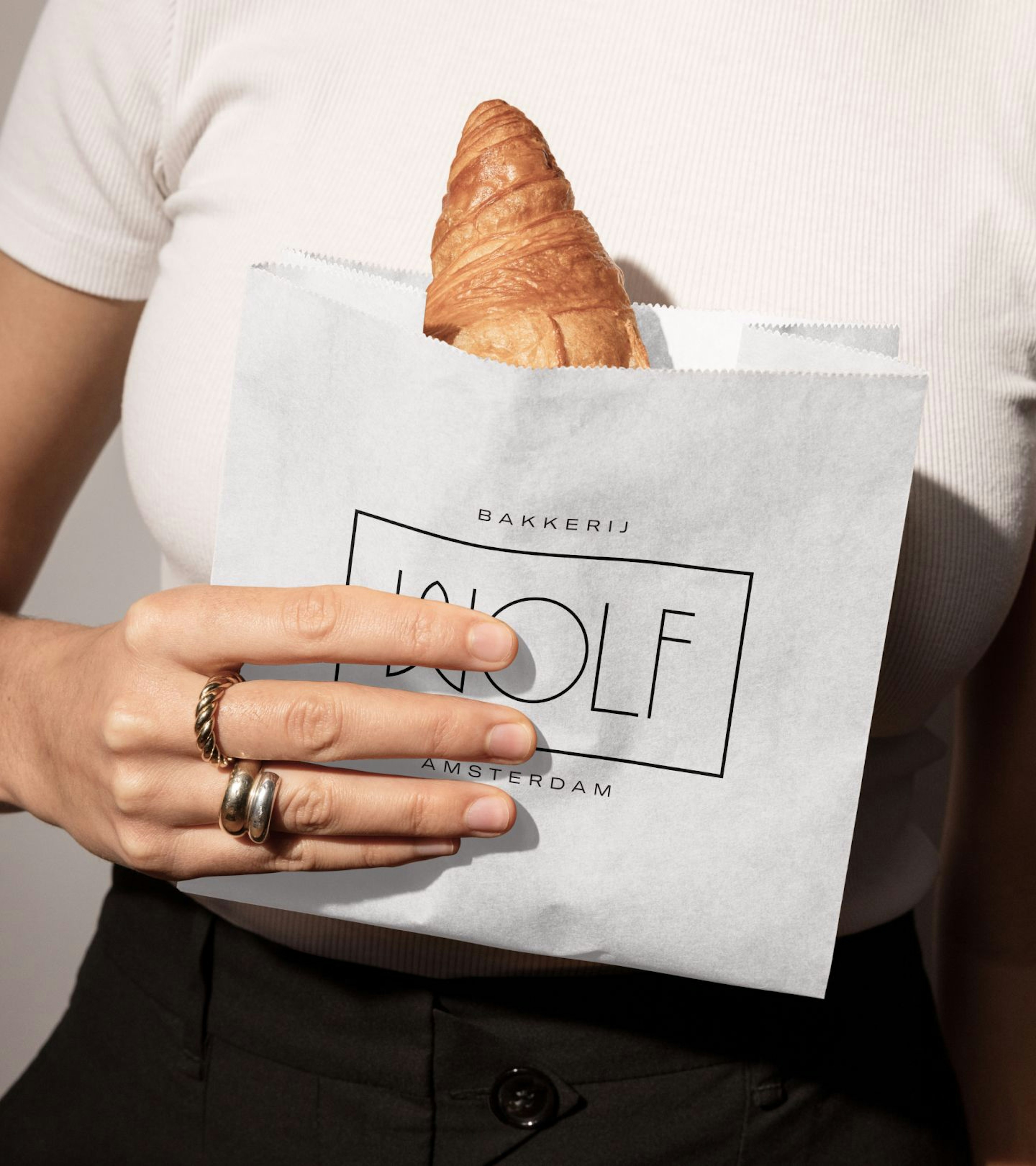 A woman wearing a white t-shirt holding a bag containing a croissant