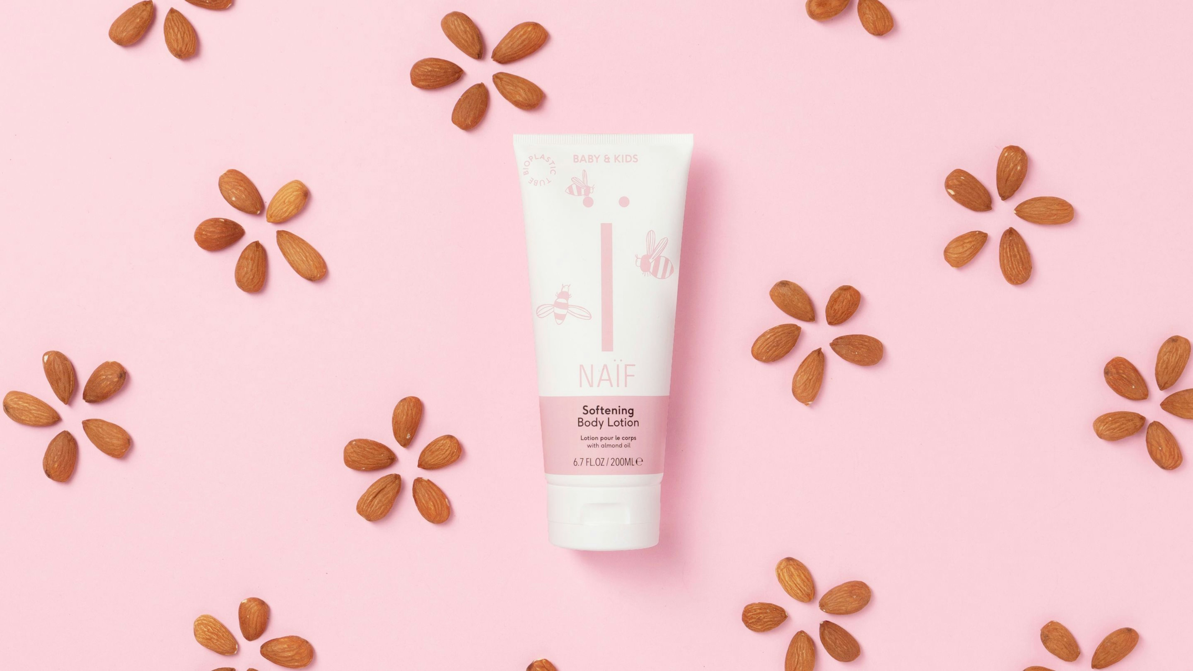 A pink background with Naïf brand softening body lotion in the foreground