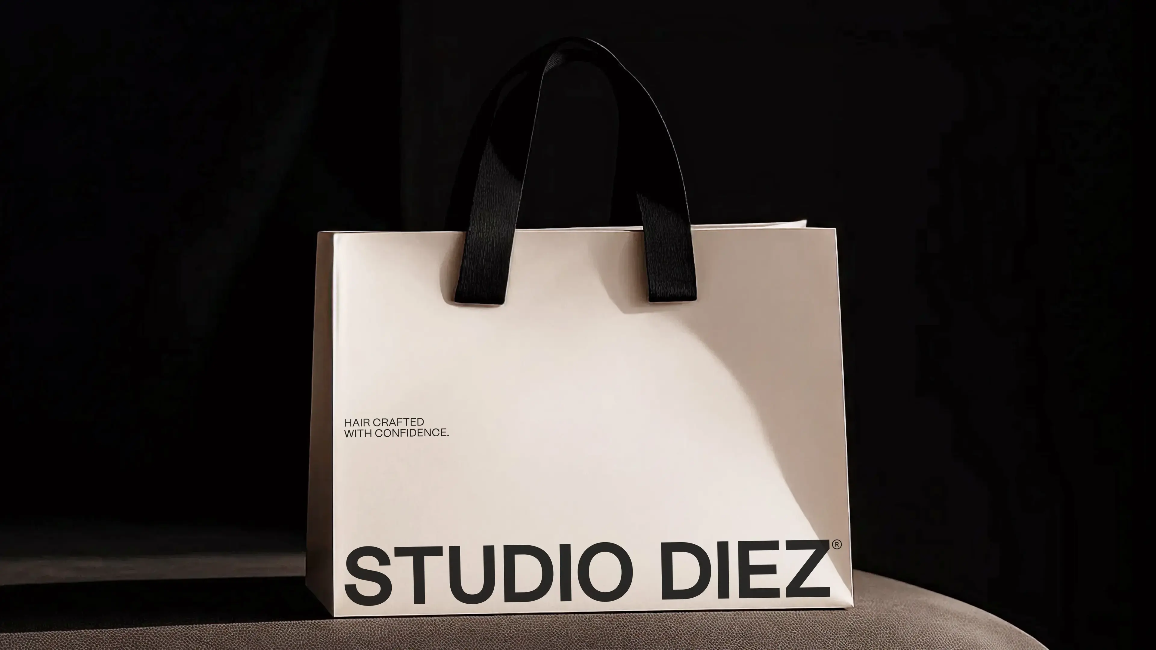 White shopping bag with black handles, featuring the text "Hair Crafted with Confidence" and "STUDIO DIEZ" on a dark background.