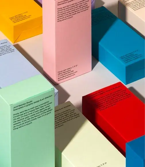 Colorful rectangular boxes in pink, blue, yellow, and red, with printed text, arranged on a white surface in bright light.