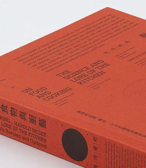 Orange book titled "On Food and Cooking: The Science and Lore of the Kitchen" by Harold McGee, featuring various texts on the cover.