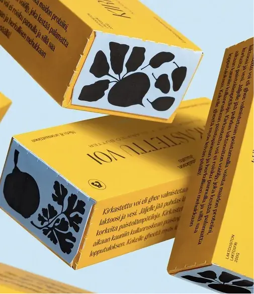 Yellow food packaging with black botanical illustrations and text, featuring a prominent round logo. Boxes appear against a light blue background.
