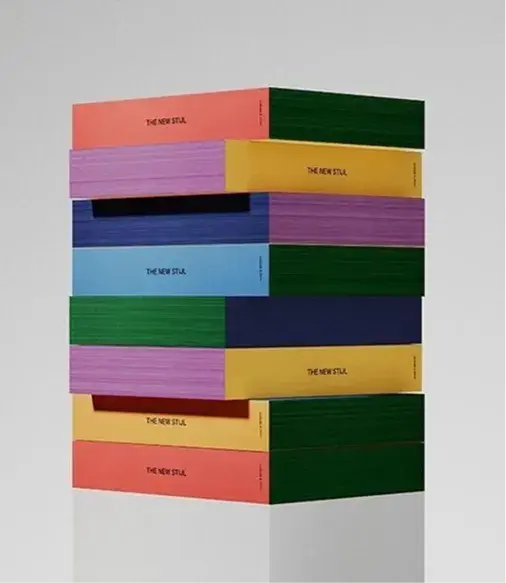 A stack of colorful books with plain covers in pink, green, and other shades. The books are labeled "The New Stil."