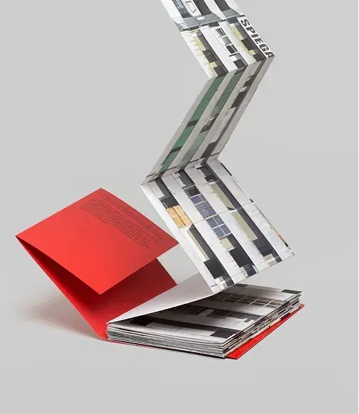 Accordion-style foldout with architectural images, attached to a partially open red-covered book on a plain background.