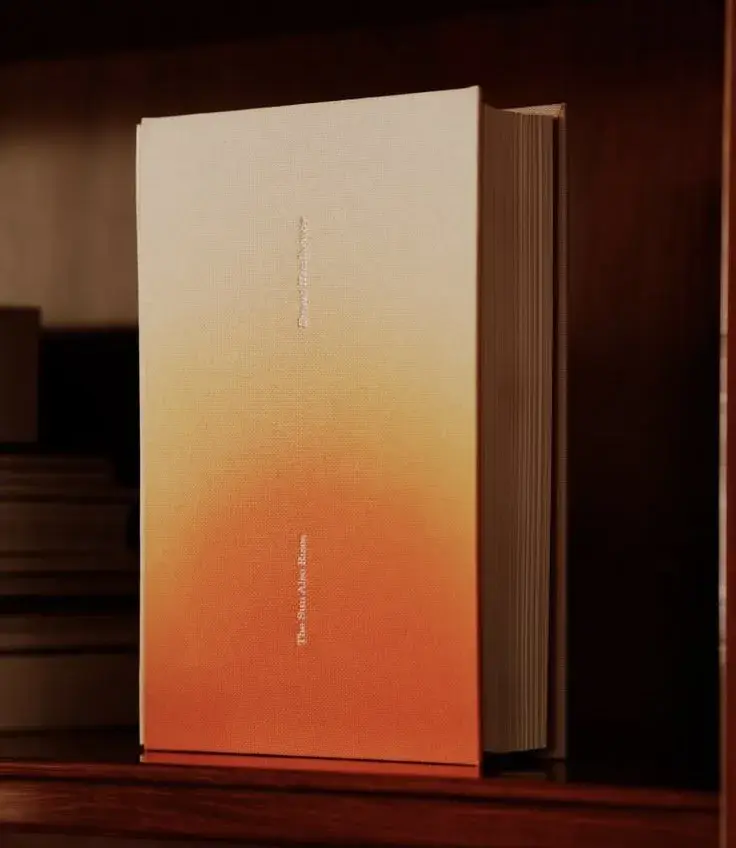 A thick book with an orange gradient cover, titled in small white text, standing upright on a wooden shelf.