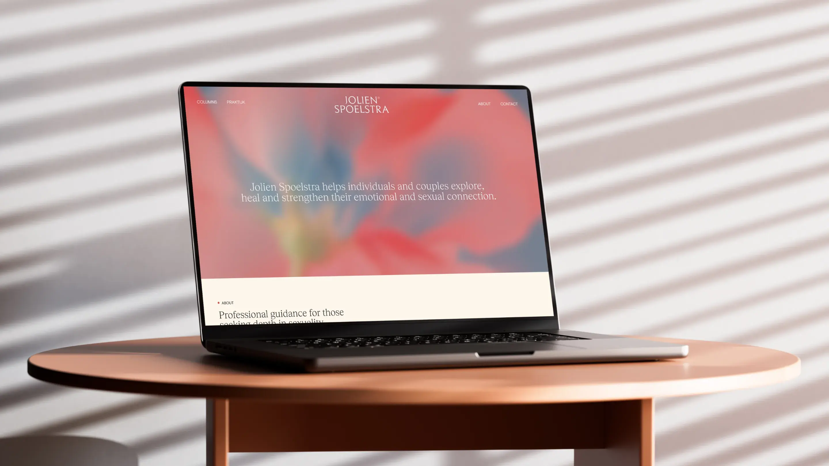 Laptop on a round table displaying a website with a blurred floral background and text about emotional and sexual connection guidance.